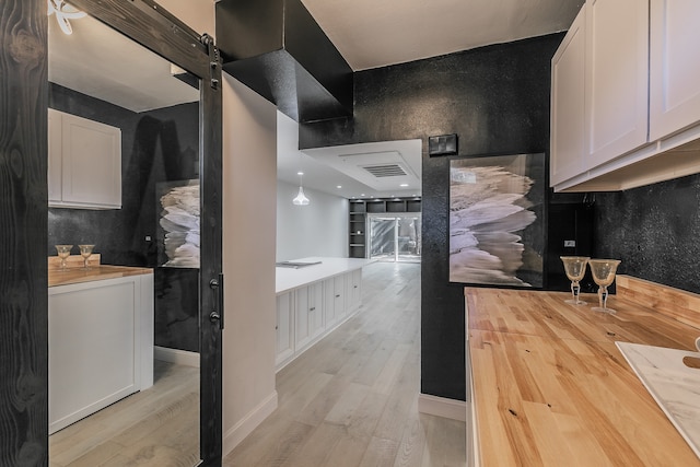 kitchen featuring butcher block counters, a barn door, pendant lighting, light hardwood / wood-style floors, and white cabinets