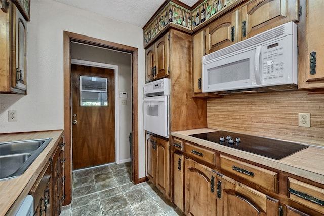 kitchen with backsplash, a textured ceiling, dark tile patterned flooring, sink, and white appliances