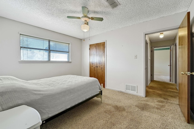 bedroom with ceiling fan, a textured ceiling, a closet, and light colored carpet