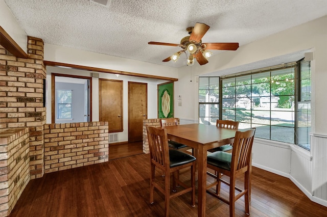 dining space with ceiling fan, dark hardwood / wood-style floors, a textured ceiling, and brick wall