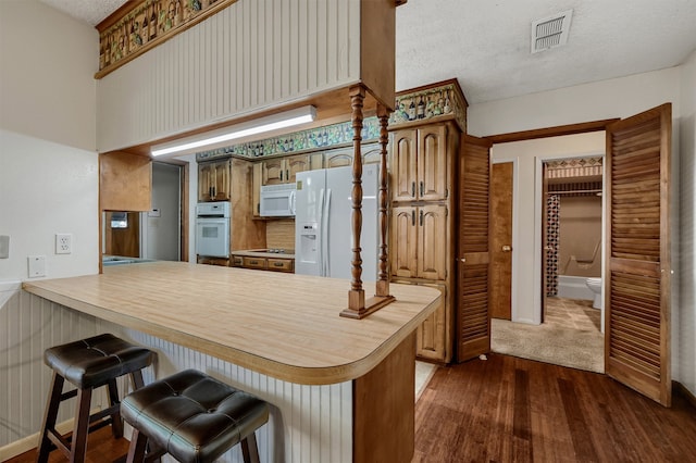 kitchen with dark wood-type flooring, white appliances, a breakfast bar area, and kitchen peninsula