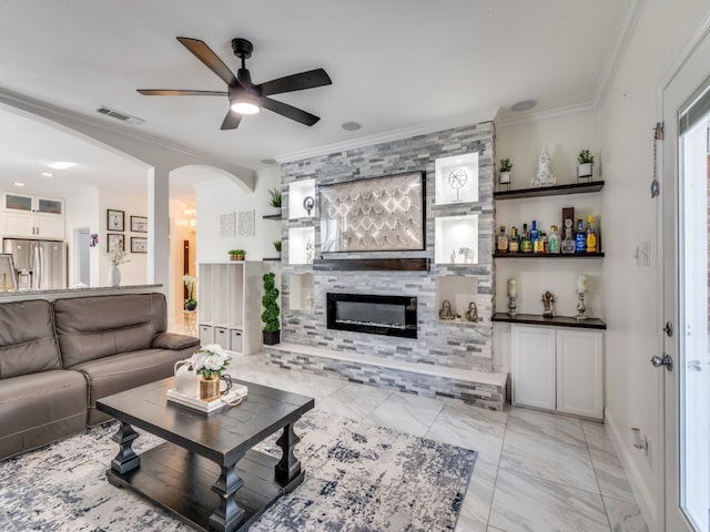 living room with ceiling fan, a large fireplace, and ornamental molding