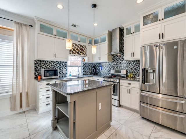 kitchen with dark stone counters, wall chimney range hood, appliances with stainless steel finishes, pendant lighting, and a center island