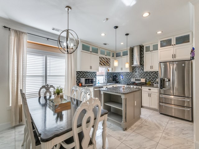 kitchen featuring stainless steel appliances, dark stone counters, a kitchen island, hanging light fixtures, and wall chimney exhaust hood