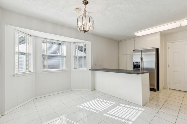 kitchen with decorative light fixtures, stainless steel fridge, kitchen peninsula, a notable chandelier, and light tile patterned floors