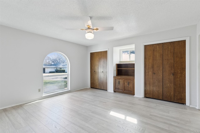 unfurnished bedroom with multiple closets, light hardwood / wood-style floors, a textured ceiling, and ceiling fan