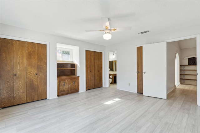 unfurnished bedroom featuring multiple closets, light hardwood / wood-style flooring, ensuite bath, and ceiling fan