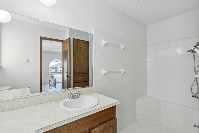 bathroom with toilet, tiled shower, a textured ceiling, and vanity