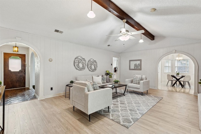 living room featuring arched walkways, light wood-style floors, a ceiling fan, a textured ceiling, and a chandelier