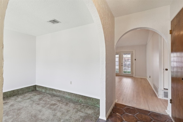 interior space featuring dark colored carpet, a textured ceiling, and french doors