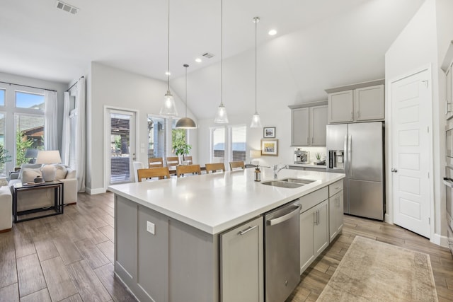 kitchen with a wealth of natural light, stainless steel appliances, gray cabinets, and an island with sink