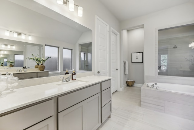 bathroom with tiled bath, tile patterned flooring, vanity, and lofted ceiling