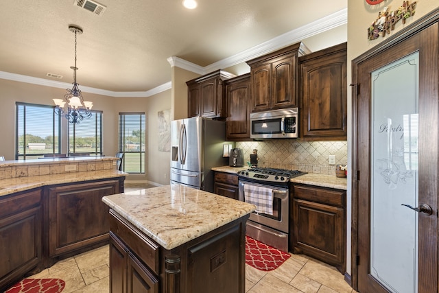 kitchen featuring decorative light fixtures, ornamental molding, appliances with stainless steel finishes, a notable chandelier, and a kitchen island