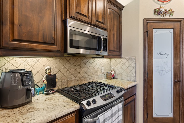 kitchen with dark brown cabinets, light stone countertops, appliances with stainless steel finishes, and tasteful backsplash