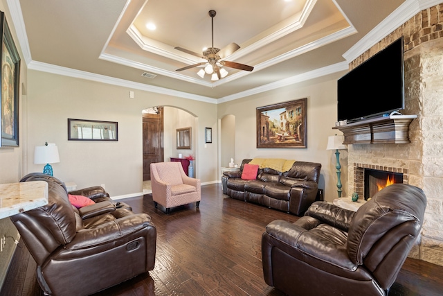 living room with a raised ceiling, a stone fireplace, dark hardwood / wood-style floors, and ornamental molding