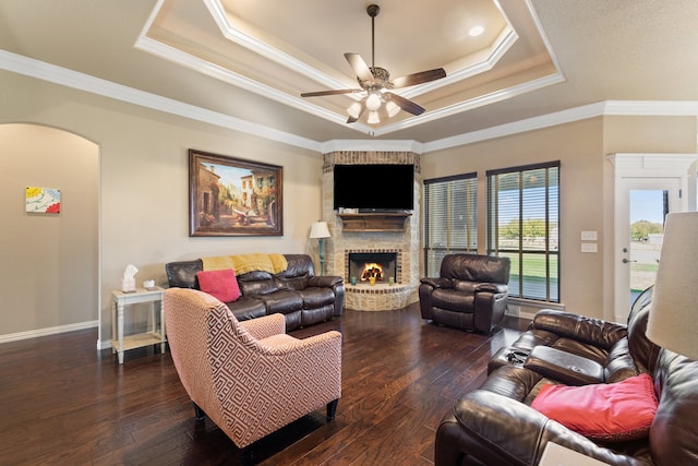 living room with dark hardwood / wood-style flooring, a brick fireplace, ornamental molding, a raised ceiling, and ceiling fan