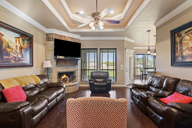 living room with a raised ceiling, crown molding, a brick fireplace, ceiling fan, and dark hardwood / wood-style flooring