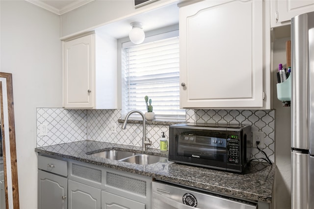 kitchen with stainless steel appliances, white cabinets, sink, ornamental molding, and dark stone countertops