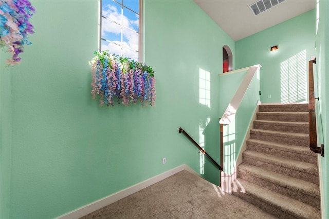 stairway featuring plenty of natural light, carpet floors, and a high ceiling