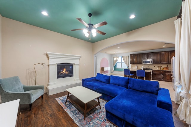 living room with dark wood-type flooring, ceiling fan, and a high end fireplace