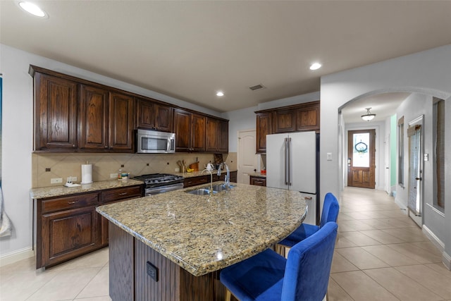 kitchen with light stone countertops, sink, a kitchen island with sink, stainless steel appliances, and decorative backsplash