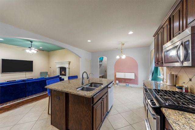 kitchen featuring dark brown cabinets, stainless steel appliances, a kitchen island with sink, sink, and hanging light fixtures