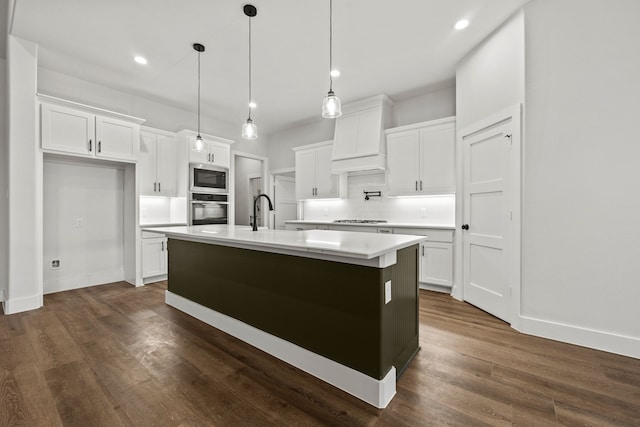 kitchen with white cabinets, light countertops, appliances with stainless steel finishes, hanging light fixtures, and a center island with sink