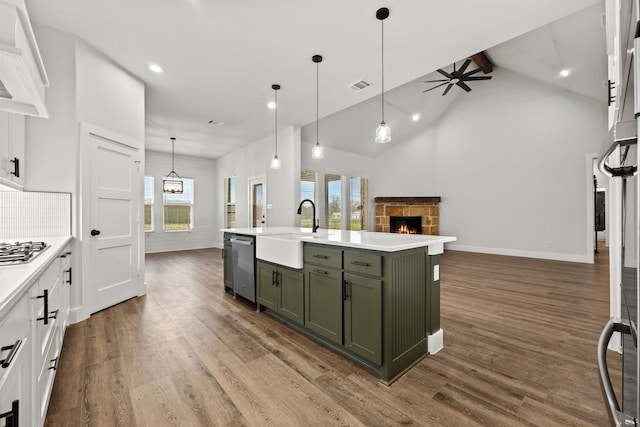 kitchen with stainless steel appliances, light countertops, open floor plan, a stone fireplace, and an island with sink