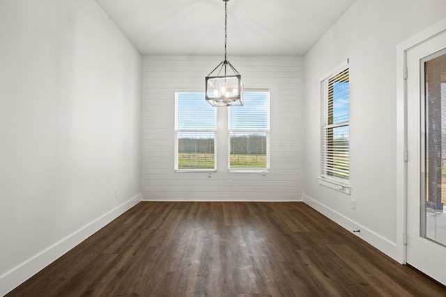 unfurnished dining area featuring a chandelier, dark wood-style flooring, and baseboards