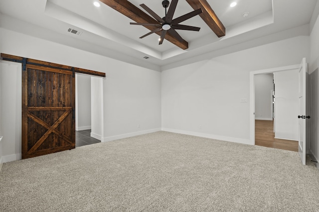 unfurnished bedroom featuring visible vents, dark carpet, a tray ceiling, and a barn door