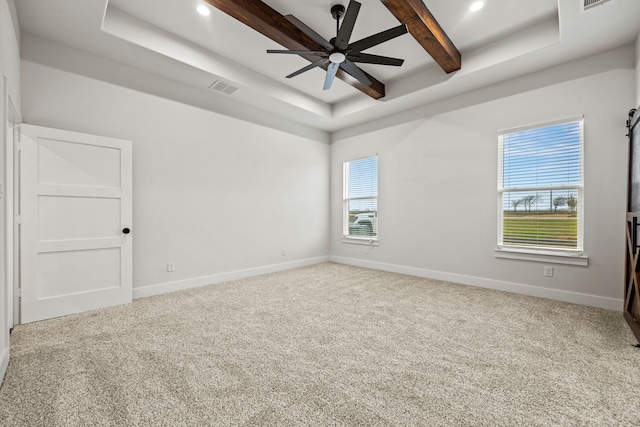 spare room featuring light colored carpet, a tray ceiling, visible vents, and baseboards