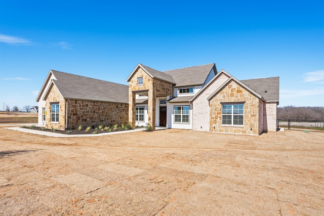 view of front of home featuring stone siding and roof with shingles