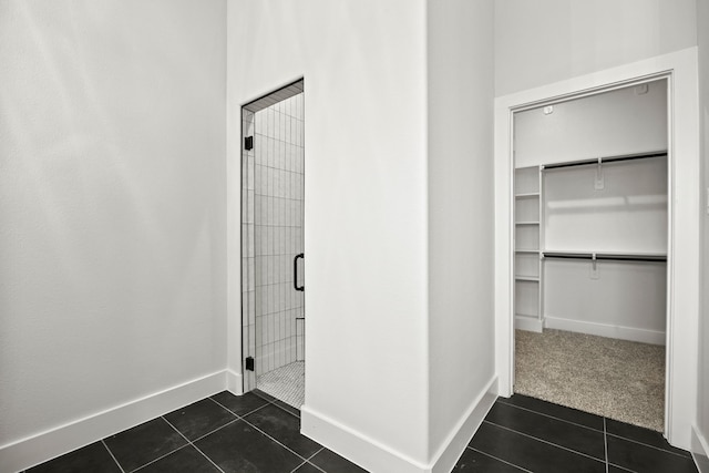 bathroom with a stall shower, a walk in closet, tile patterned flooring, and baseboards