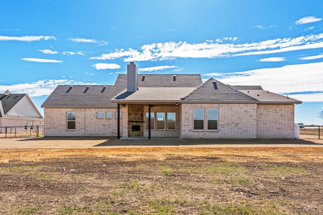 rear view of property with roof with shingles, brick siding, a patio, a chimney, and fence