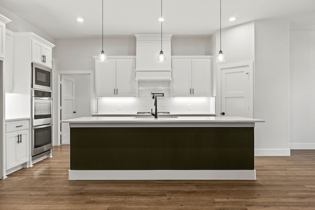 kitchen featuring hanging light fixtures, a center island with sink, white cabinetry, and light countertops