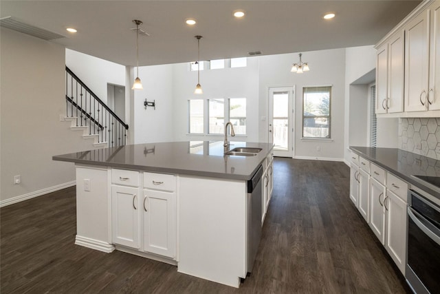 kitchen featuring white cabinets, decorative light fixtures, stainless steel appliances, sink, and a center island with sink