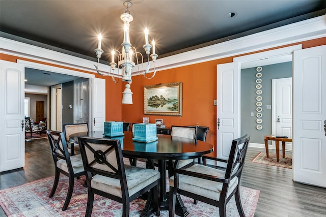 dining area featuring dark wood-type flooring, ornamental molding, and an inviting chandelier