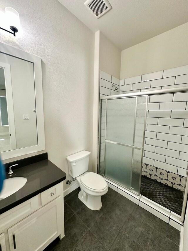 bathroom with tile patterned flooring, a shower with door, vanity, and toilet