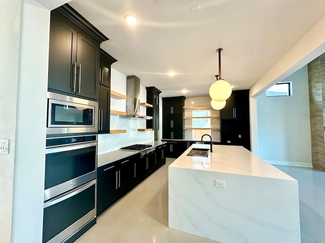 kitchen featuring a center island with sink, wall chimney range hood, hanging light fixtures, sink, and appliances with stainless steel finishes