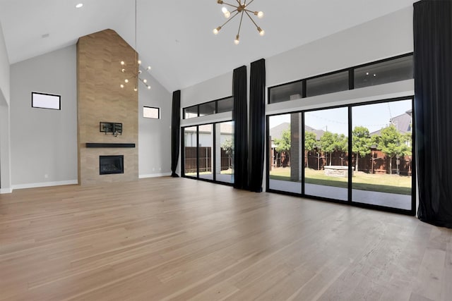 1719 Silver Marten Trl, Arlington, TX 76005 - unfurnished living room featuring baseboards, a chandelier, a tiled fireplace, high vaulted ceiling, and light wood finished floors