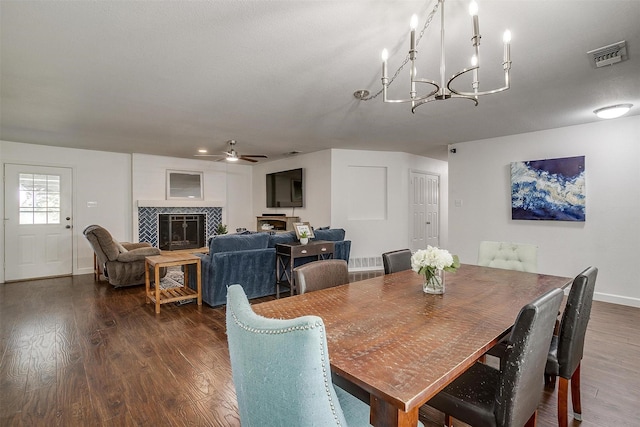 dining room with dark wood-type flooring, ceiling fan with notable chandelier, and a fireplace