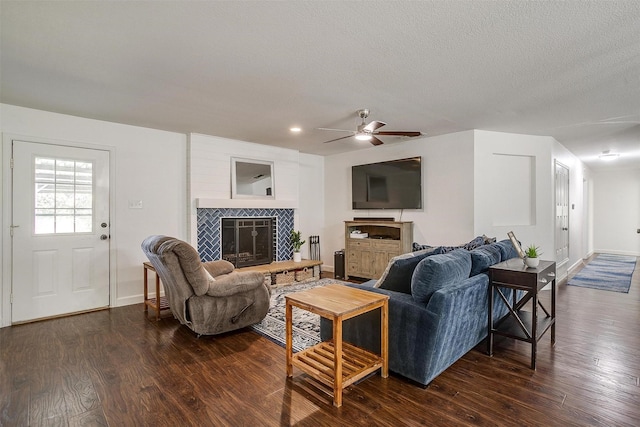 living room with ceiling fan, dark hardwood / wood-style flooring, a tiled fireplace, and a textured ceiling