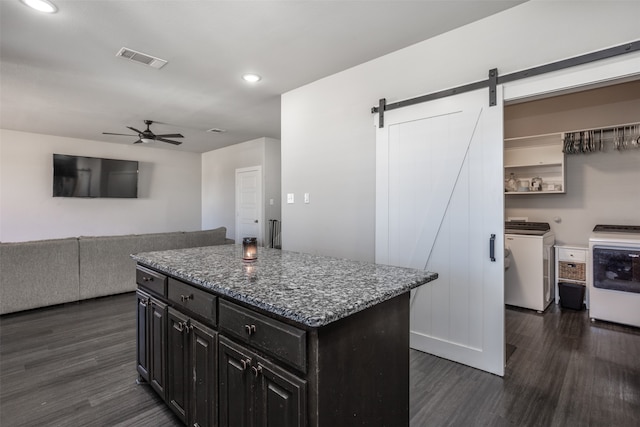 kitchen featuring dark hardwood / wood-style floors, ceiling fan, a center island, a barn door, and washing machine and dryer