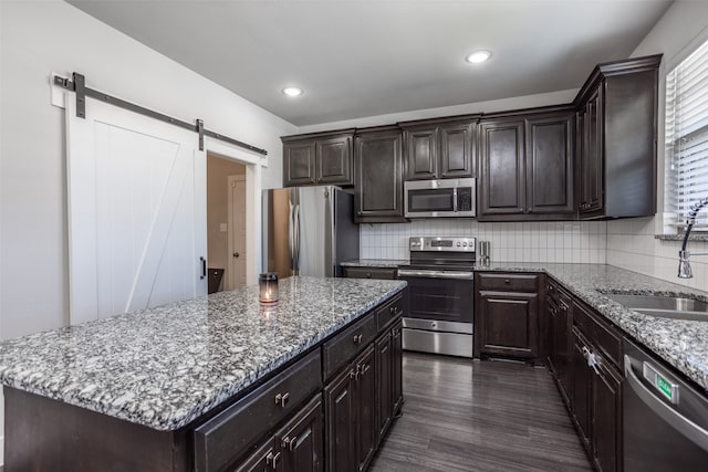 kitchen featuring a center island, a barn door, backsplash, light stone countertops, and appliances with stainless steel finishes