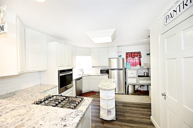 kitchen featuring stainless steel appliances, white cabinetry, sink, light stone counters, and dark wood-type flooring