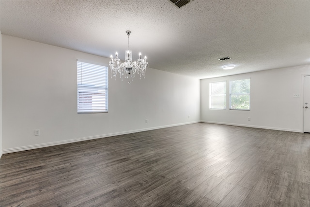 empty room featuring a chandelier, a textured ceiling, and dark hardwood / wood-style floors