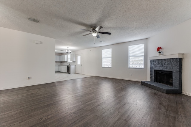 unfurnished living room with a fireplace, dark hardwood / wood-style flooring, a textured ceiling, and ceiling fan with notable chandelier