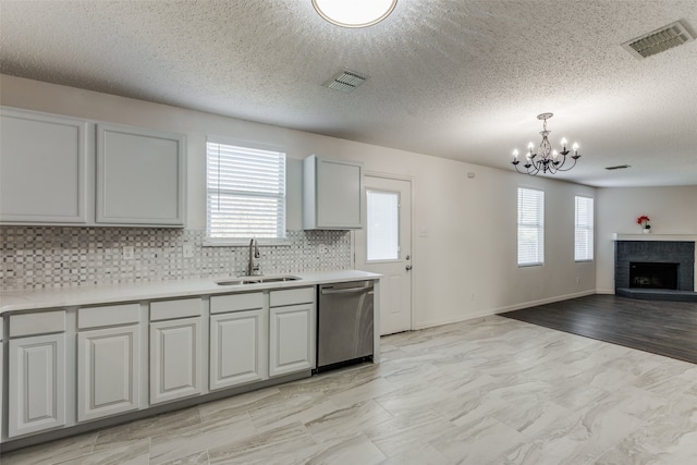 kitchen with a brick fireplace, hanging light fixtures, sink, tasteful backsplash, and stainless steel dishwasher