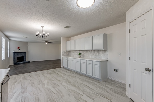 kitchen with a brick fireplace, light hardwood / wood-style floors, ceiling fan with notable chandelier, and a textured ceiling