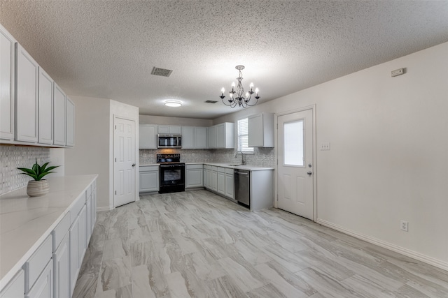 kitchen with stainless steel appliances, light stone counters, a textured ceiling, a chandelier, and pendant lighting